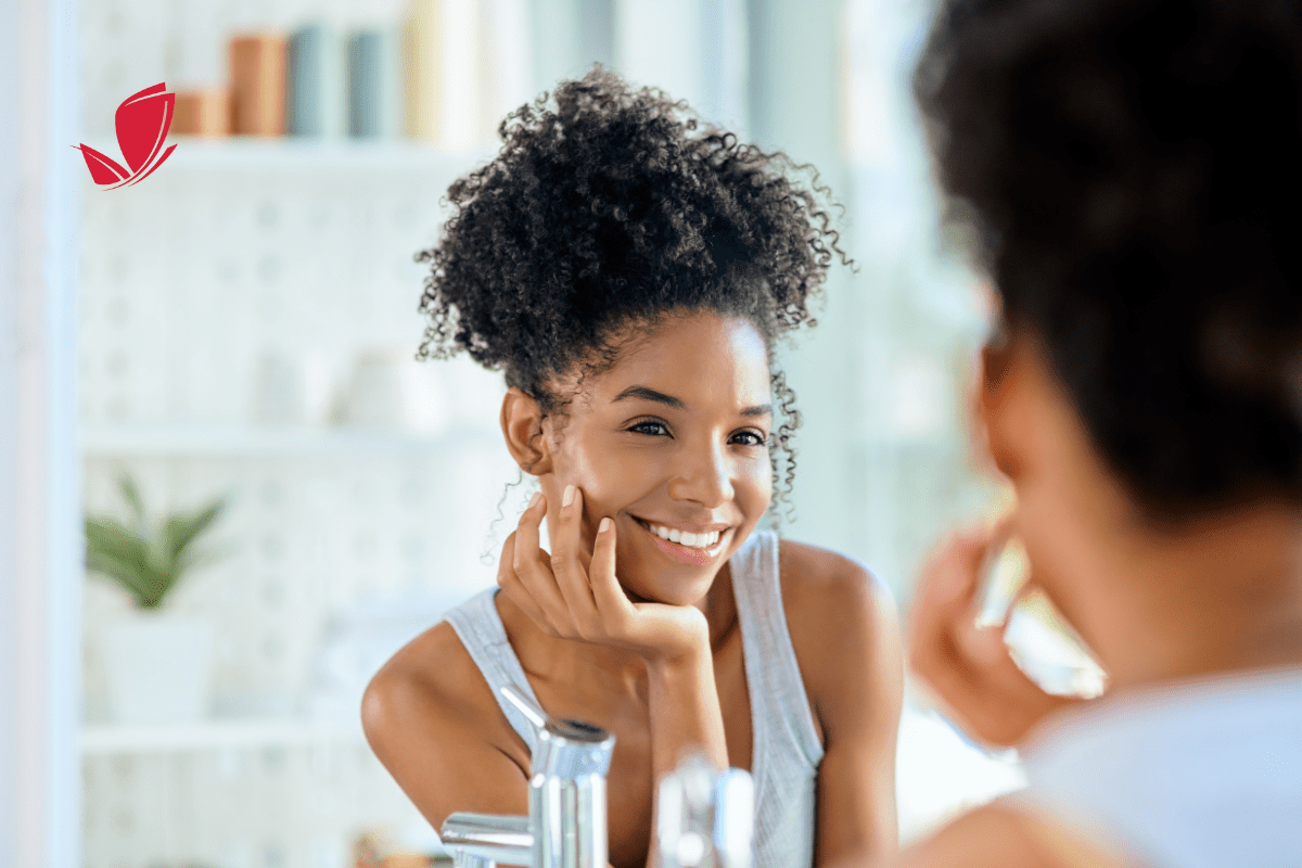 Young woman looking in the mirror using skin care and smiling.