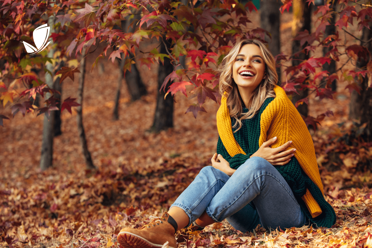 girl in woods wearing a sweater sitting on leaves