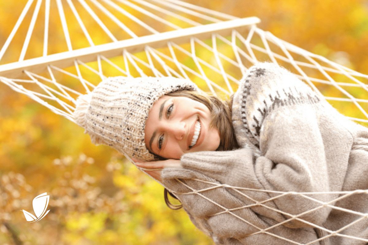 woman in a knit hat, laying on a hammock in the fall.